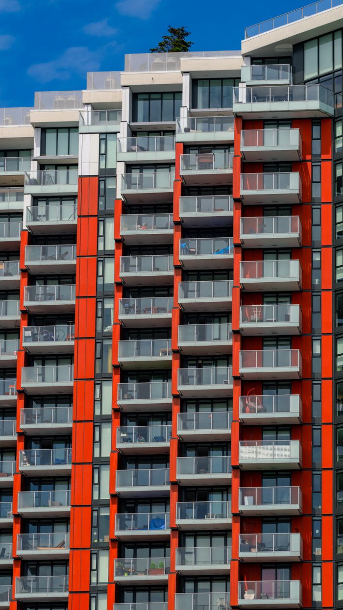 Vertical shot of a modern apartment building with bold red panels and numerous balconies under clear blue sky.